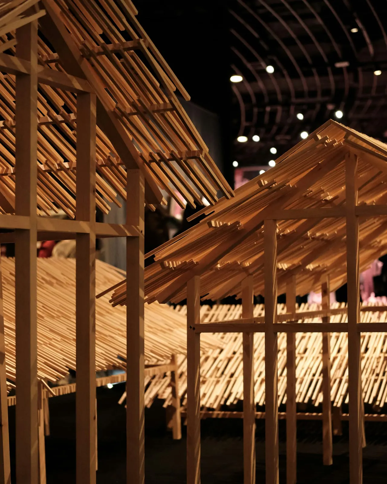 Exposición con pabellones de listones de madera y tejado a dos aguas bajo una luz cálida
