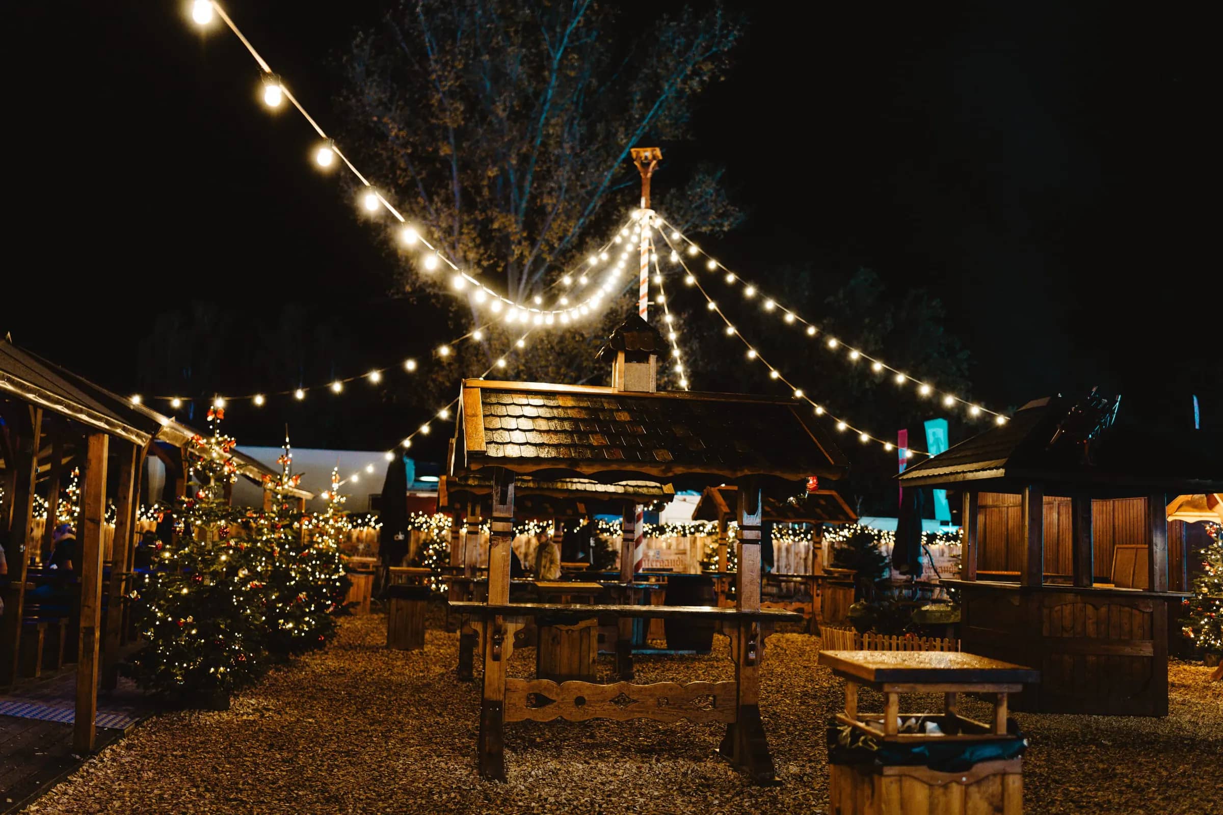Mercado navideño de noche con casetas de madera y guirnaldas de luces